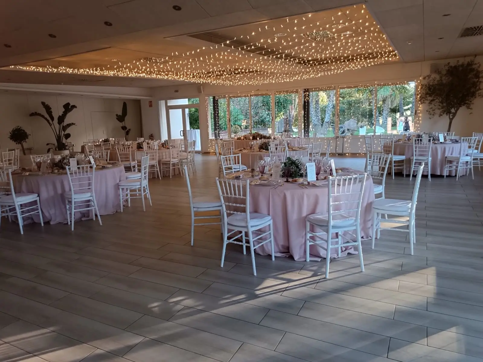 El salón con el techo cubierto de luces pequeñas, mesas redondas de mantel rosa pálido y sillas blancas